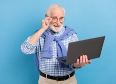 Photo of optimistic old grey hairdo man hold laptop wear spectacles blue shirt isolated on pastel color background